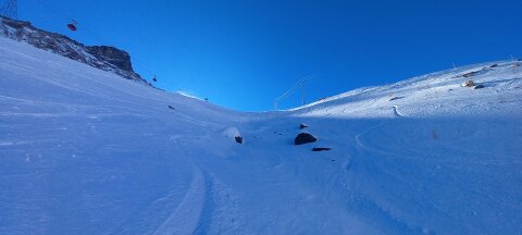 Épp egy patak völgy van a hó alatt, balra a Felskinn Bahn