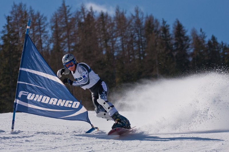 A fotót hason fekve készítettük, a pálya helyett az erdő szerepel a snowboardos mögött a háttérben, így jobban érvényesül a kanyar közben fröccsenő hó. A blendét nyitva használva a háttér elmosódott, így még jobban elkülönül a versenyző a környezetétől.